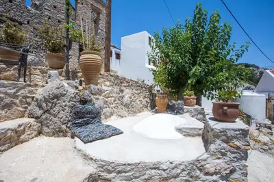 a stone patio with two chairs and a tree at kalosymi studio, Symi in Symi