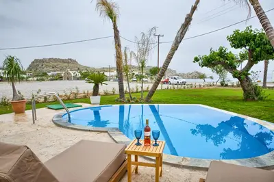 a blue swimming pool with a bottle of wine on a table at Le Palme Beach Rhodes in Haraki