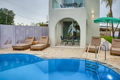 a house with a swimming pool with chairs and an umbrella at Le Palme Beach Rhodes in Haraki