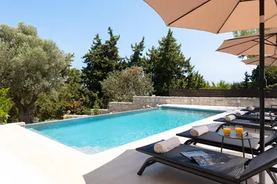 a swimming pool with two chairs and an umbrella at Villa Olive in Koskinou