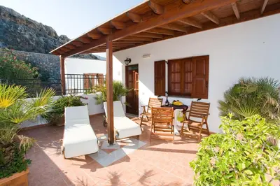 a patio with white chairs and a wooden pergola at Anastasia Studios Lindos in Líndos