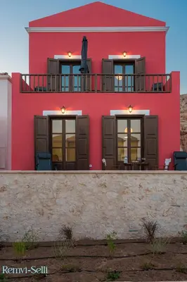 a red building with chairs on the balcony at Remvi Seaside Houses in Halki