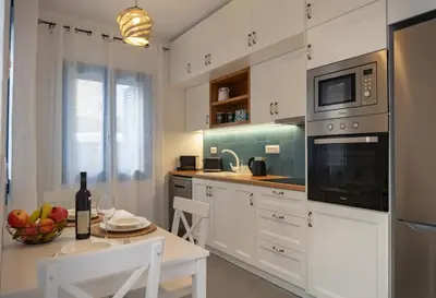 a kitchen with white cabinets and a table with a bowl of fruit at Diolanth traditional house in Koskinou