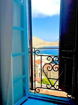 an open window of a balcony with a view of a house at Maestro apartment Chalki in Halki