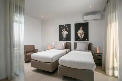 two twin beds in a room with a couch and paintings at Villa Lily in Pefki Rhodes