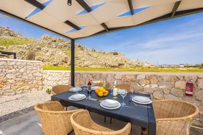 a patio with a table and chairs and a stone wall at Villa 12 Chado in Kolimbia