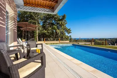 a swimming pool with wicker chairs next to a house at Louloudi Hills Villa 1 in Koskinou