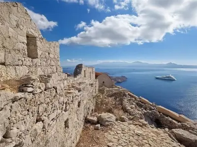 a cruise ship in the water behind a stone wall at Yellow Oasis traditional home with sea view in Halki