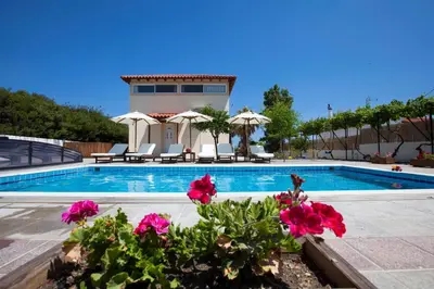 a swimming pool with pink flowers in front of a house at Villa Nefeli in Kiotari