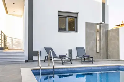 a swimming pool with two chairs next to a house at Ramo Luxury Villa in Kremasti