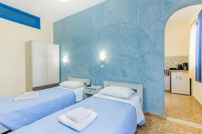 two beds in a room with a blue wall at Vassos Apartments in Líndos