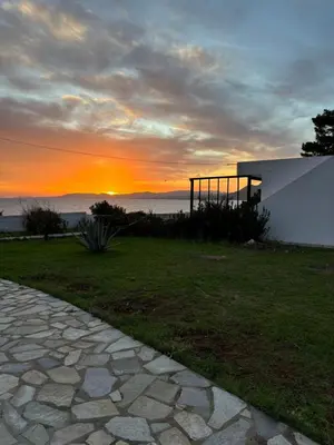 a sunset behind a house with a stone walkway at Amphora Sea View Pefkos in Pefki Rhodes