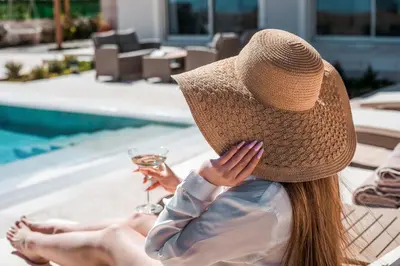 a woman wearing a straw hat sitting next to a pool at Aeon Rhodes - New Villa with private pool in Rhodes Town