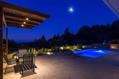 a patio with a table and chairs and a swimming pool at night at Villa Anastazia in Koskinou