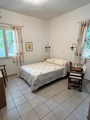 a bedroom with a bed and a table and two windows at Summerhouse Marianna in Ixia