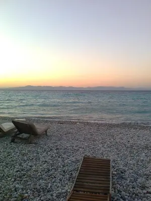 a beach with a bench and the ocean at sunset at Summerhouse Marianna in Ixia