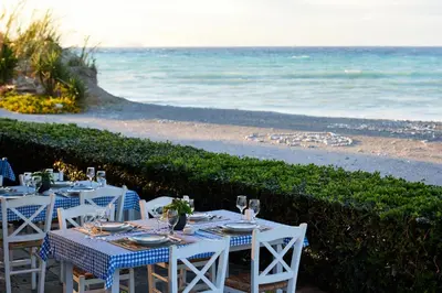 two tables with plates and wine glasses on the beach at Blue Bay Beach Resort in Ialyssos