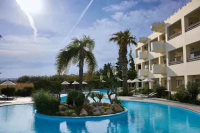 a resort swimming pool with palm trees and a building at Blue Bay Beach Resort in Ialyssos