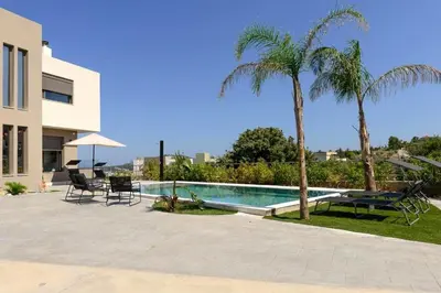 a swimming pool with two chairs and two palm trees at Aetheria Luxury Villa in Kalithies