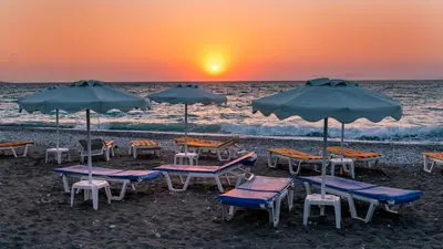 a group of chairs and umbrellas on the beach at sunset at Sirene Beach Hotel in Ixia