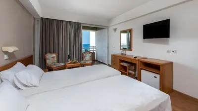 a hotel room with a bed and a desk and a television at Sirene Beach Hotel in Ixia