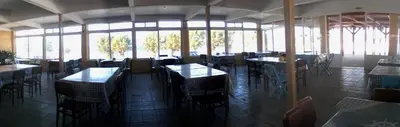a dining room with tables and chairs and windows at To Akrogiali in Phanaes