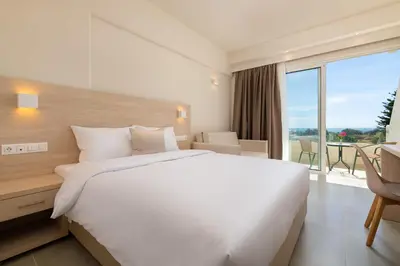 a bedroom with a large white bed and a large window at Afandou Bay Village Resort Hotel in Afantou