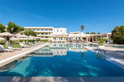 a swimming pool with chairs and a hotel in the background at Afandou Bay Village Resort Hotel in Afantou