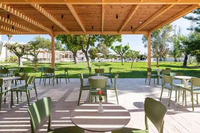 a patio with tables and chairs in a park at Afandou Bay Village Resort Hotel in Afantou