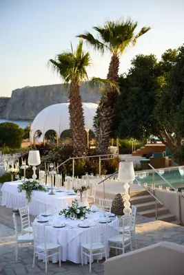 a table with white tables and chairs and palm trees at Palazzo Navarone in Líndos