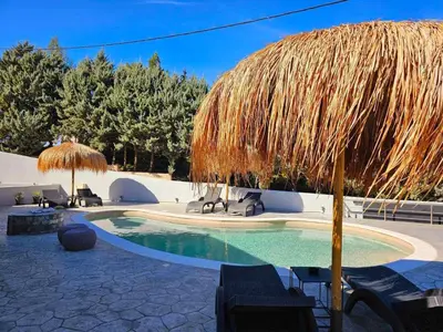 a swimming pool with a straw umbrella and chairs at Dream Luxury Suites & Apartment Pastida in Pastida