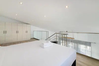 a white bedroom with a large bed and a staircase at Stone Apartments in Kremasti
