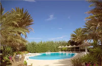 a large swimming pool with palm trees and chairs at Paras Beach Apartments in Ialyssos