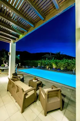 a patio with chairs and a pool at night at Filerimos Oasis Villa in Ialyssos