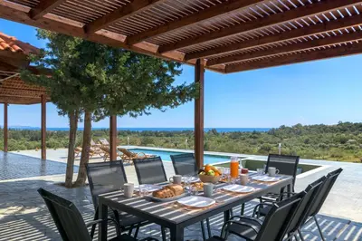 a dining table and chairs under a pergola next to a pool at ElaionHill-villa in Gennadi