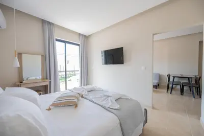 a white bedroom with a bed and a large window at Blue Wave Suites - Ixia in Ialyssos