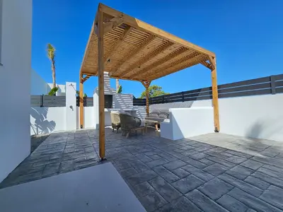 a patio with a wooden pergola on a white wall at Myrteni Pool Villas in Ialyssos
