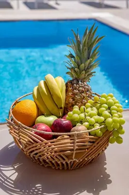 a basket of fruit on a table next to a pool at Villa Petalutha Rhodes in Kolimbia