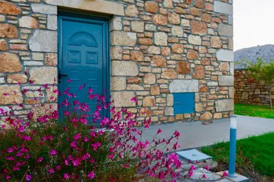 a stone building with a blue door and purple flowers at Estrella Villas in Lardos