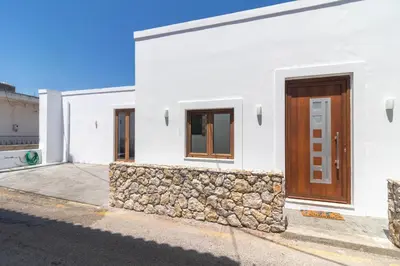 a white house with a stone wall and a wooden door at Antonis Traditional House in Afantou