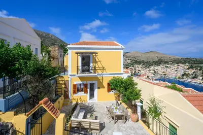 a yellow house with tables and chairs on a balcony at Elpidas Apartments in Symi