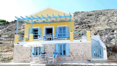 a yellow and blue house with chairs and an umbrella at Villa Panorama in Halki
