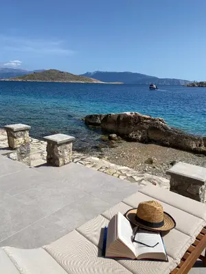 a hat and book sitting on a table next to the ocean at NUMĒNIA Seafront Property in Halki