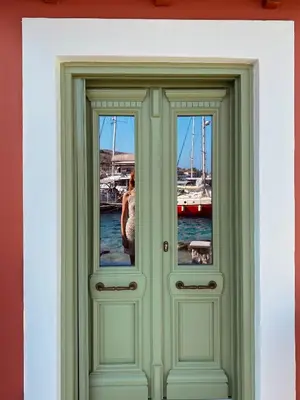 a woman is standing behind two glass doors at NUMĒNIA Seafront Property in Halki