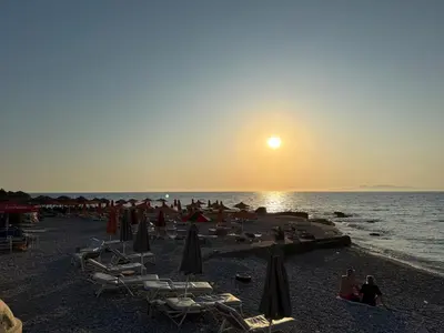 a beach with chairs and umbrellas at sunset at Polikseni Apartment Orfanidou in Rhodes Town