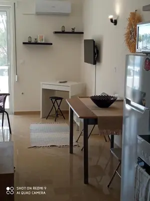 a living room with a table and a refrigerator at Beach Sunset Apartment Ialisos in Ialyssos