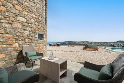 a patio with chairs and a table and a stone wall at Aitheria Lindos Villa in Líndos