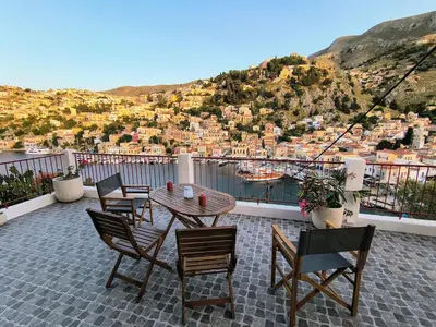 a patio with chairs and a table with a view of a city at Lirenou Scala Vista in Symi