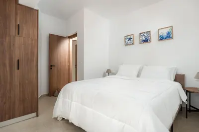 a white bedroom with a white bed and a wooden cabinet at Casa Stefania in Faliraki