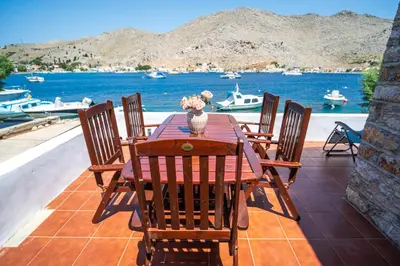 a wooden table and chairs on a patio with a view of the water at Mythos House - Seaside Retreat in Pedi in Symi